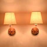 Illuminated Milan copper antique brass wall sconces with natural linen fabric shades producing a warm ambient glow, displayed in a symmetrical front-facing arrangement.
