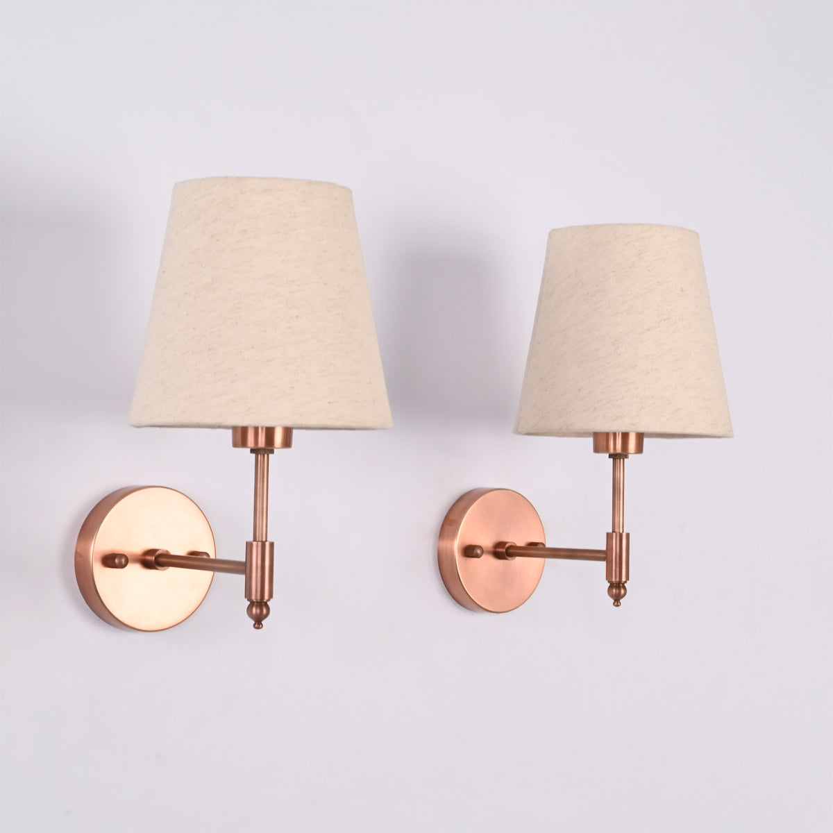 Pair of Milan natural linen shade wall sconces with handcrafted copper antique brass finish shown from a side angle, emphasizing the slim wall arm and round backplate.