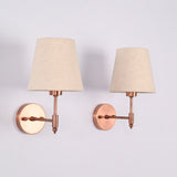 Pair of Milan natural linen shade wall sconces with handcrafted copper antique brass finish shown from a side angle, emphasizing the slim wall arm and round backplate.