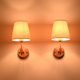 Front view of two Milan copper antique solid brass wall sconces with natural linen tapered shades illuminated to create soft, warm ambient lighting for modern and transitional interiors.
