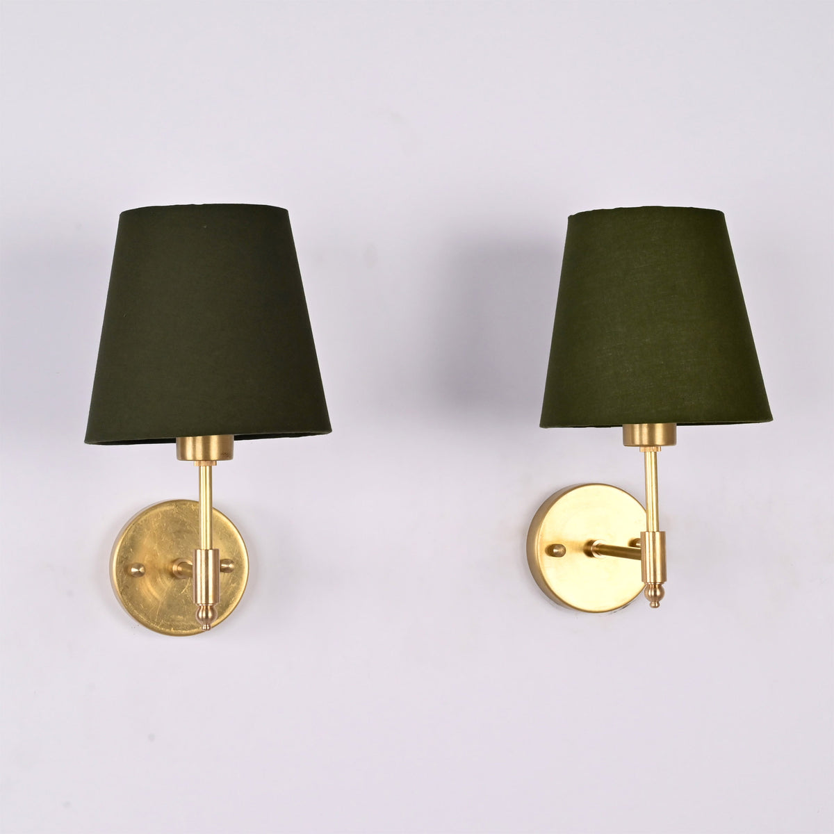 Front view of a pair of Milan brushed brass wall sconces with olive green fabric shades installed on a white wall.