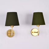 Front view of a pair of Milan brushed brass wall sconces with olive green fabric shades installed on a white wall.