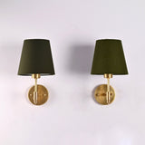 Front view of the Milan olive green fabric shade brushed brass wall sconce featuring a handcrafted solid brass frame and round wall backplate.