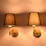 Side angle view of illuminated Milan brushed brass wall sconces with olive green tapered fabric shades showcasing warm ambient lighting.