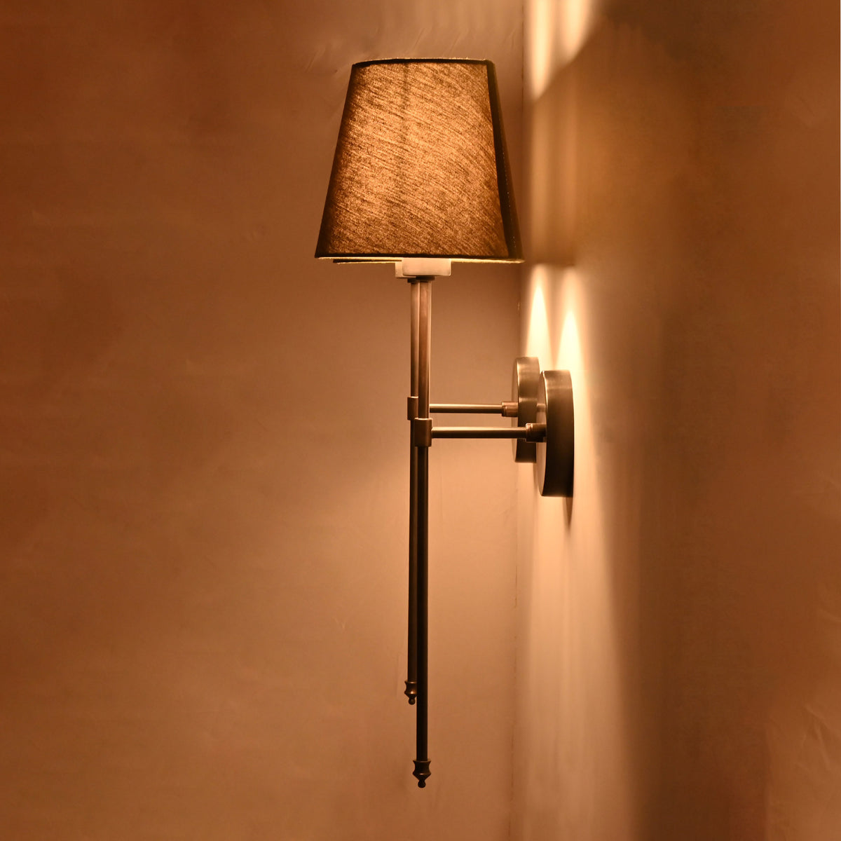 Side angle of olive shade black rod wall sconce showing warm glow and slim wall projection.