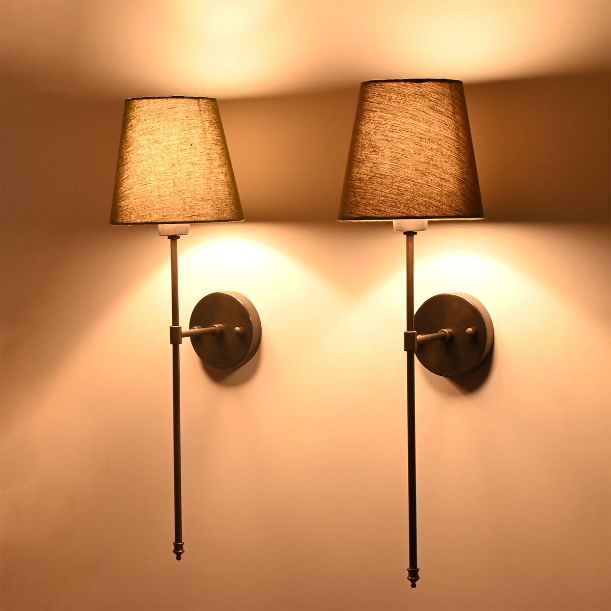 Angled pair of Milan olive shade wall sconces with black finish and warm ambient lighting effect.