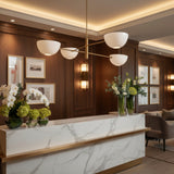 Milan 4-light chandelier with white opal bowl shades and warm brass asymmetric arms, angled product view.