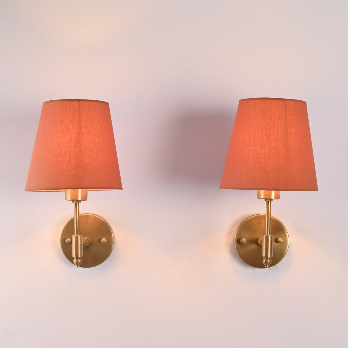 Front view of Milan Peach Shade Antique Brass Short Wall Sconce featuring a soft peach tapered fabric shade and handcrafted antique brass backplate.