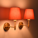 Close side view of Milan Peach Shade Antique Brass Short Wall Sconce with warm illuminated peach fabric shade and antique brass frame.