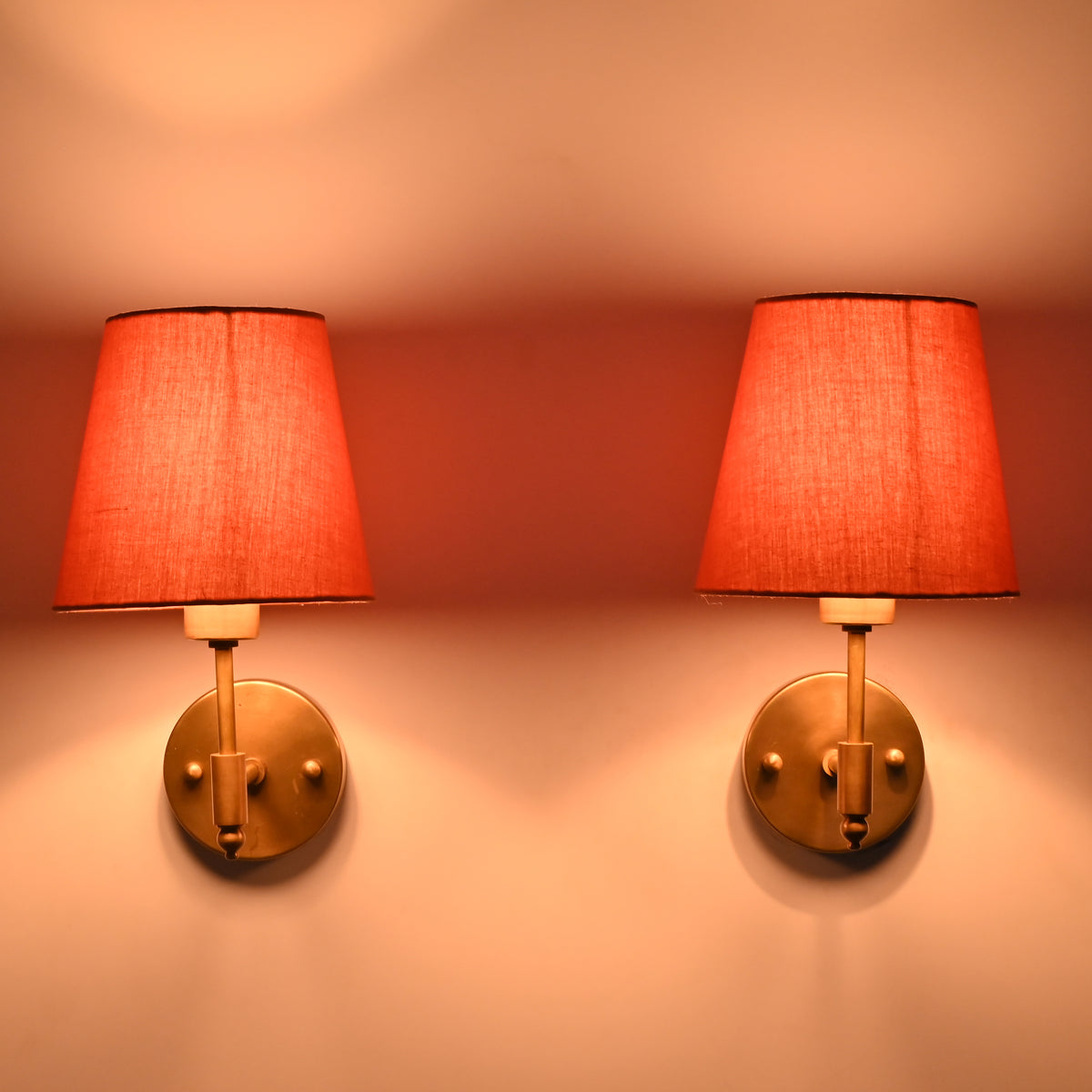 : Illuminated Milan Peach Shade Antique Brass Short Wall Sconce casting a soft warm glow through the peach fabric shade.
