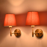 Side view of illuminated Milan Peach Shade Antique Brass Short Wall Sconce highlighting its warm ambient lighting and antique brass finish.
