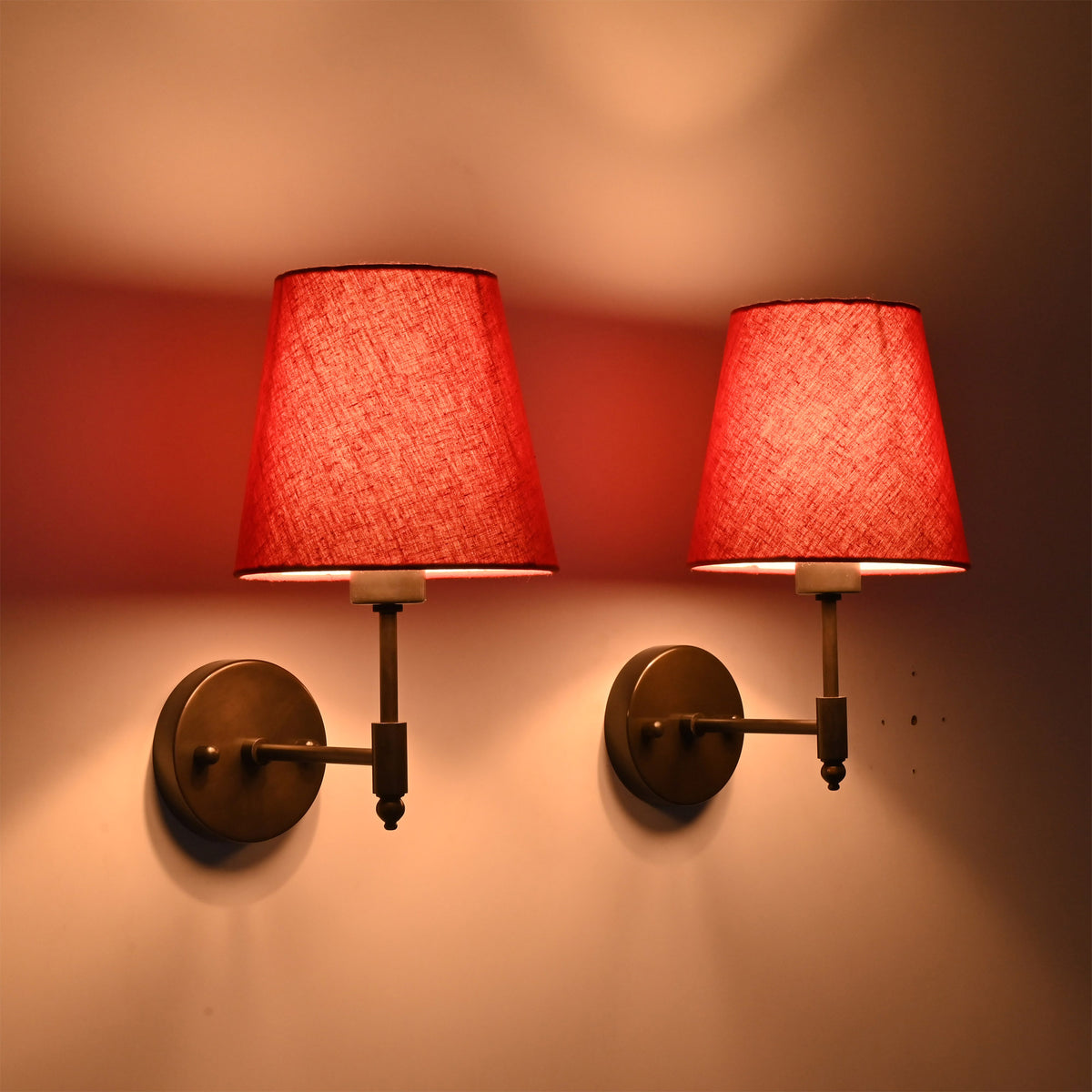 Angled pair view of Milan red shade black wall sconces with warm ambient light and compact round backplates.