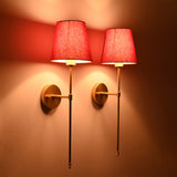 Angled view of Milan red shade wall sconces with long decorative rod and warm evening light effect.