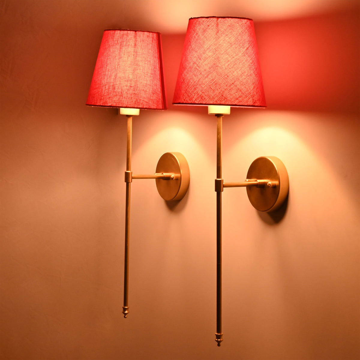 Red fabric shade wall sconces glowing warmly on wall with slim rod frame and classic round backplate.