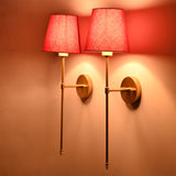 Red fabric shade wall sconces glowing warmly on wall with slim rod frame and classic round backplate.