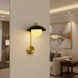 Illuminated Milan wall sconce with warm glowing glass globe, black ribbed dome shade and brass frame.