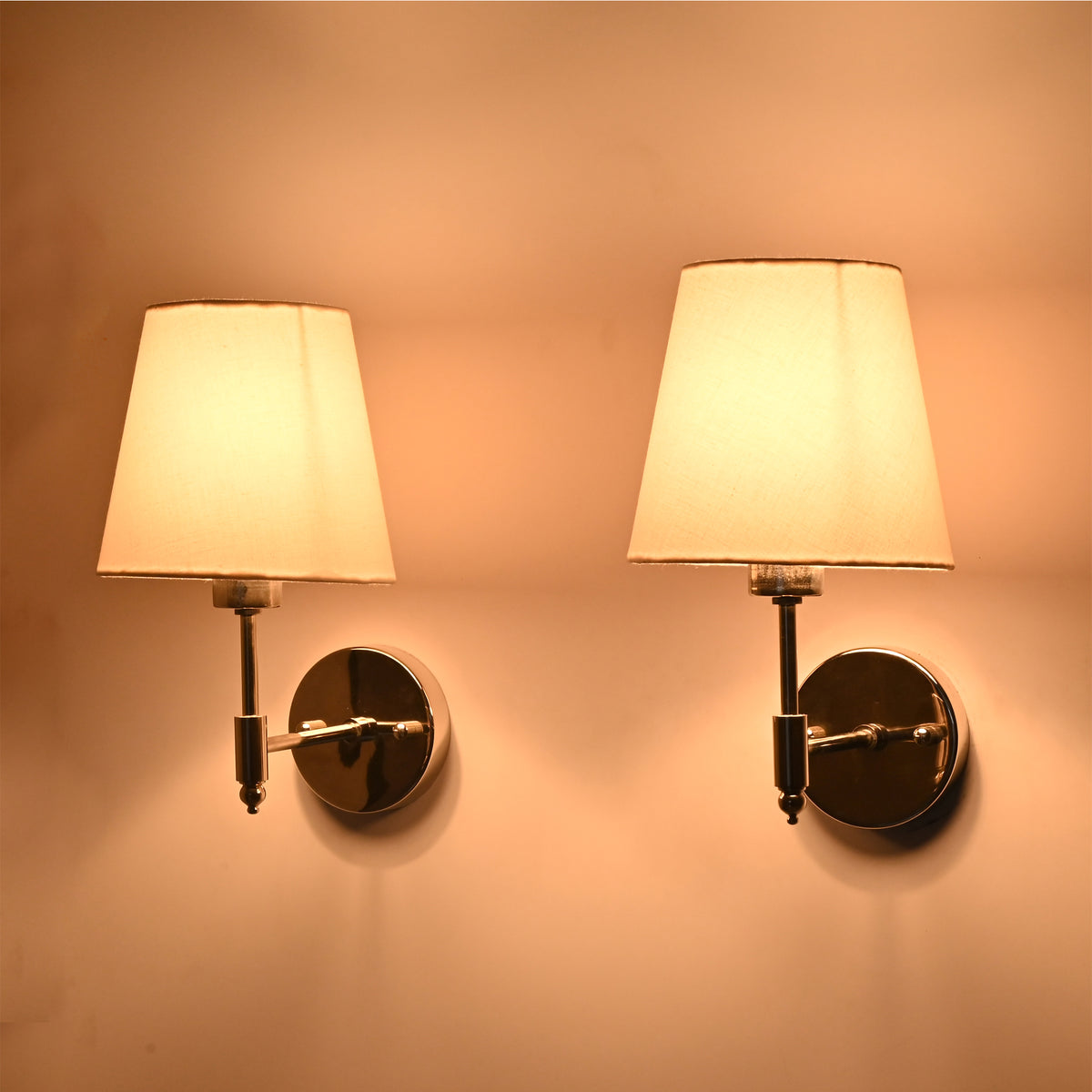 Warm illuminated angled view of Milan polished chrome wall sconces with white tapered fabric shades, ideal for luxury bedrooms and hallways.