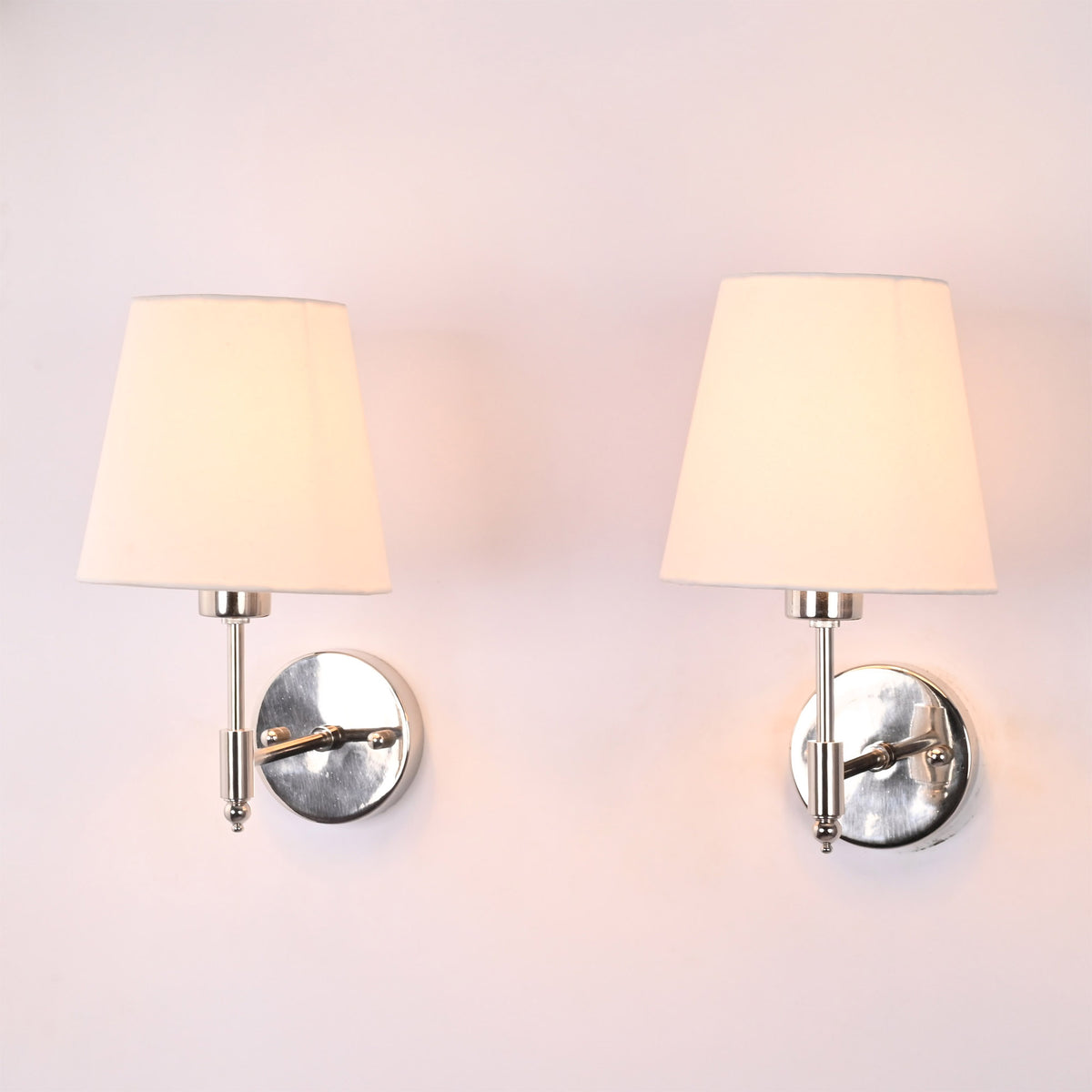 Milan polished chrome wall sconces with white fabric shades installed on a wall, showcasing clean contemporary styling in natural daylight.