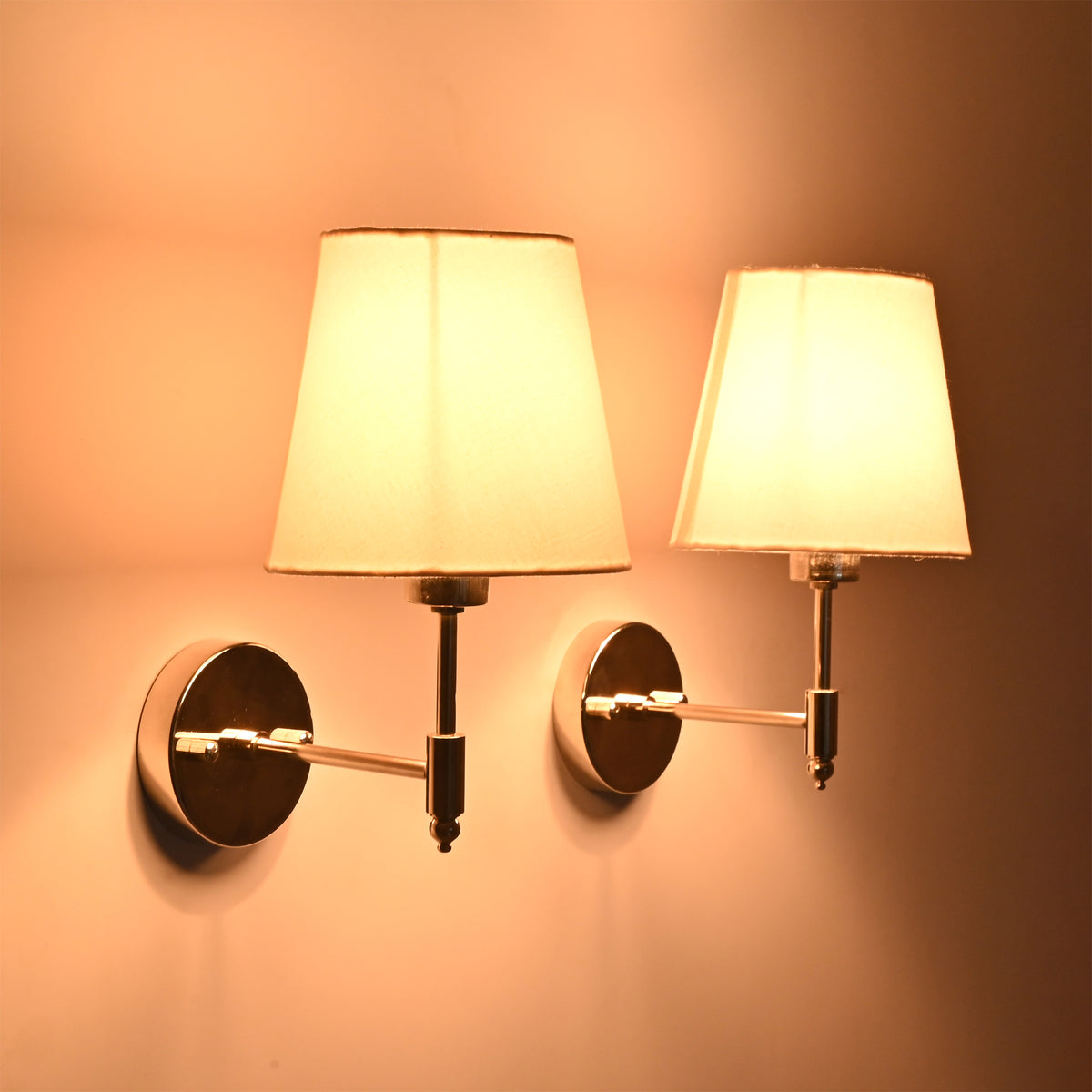 Milan polished chrome wall sconce with white tapered fabric shade illuminated, handcrafted solid brass hardwired wall light for modern bedroom, hallway, and living room.