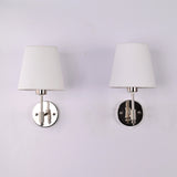 Pair of Milan polished chrome wall sconces with white tapered fabric shades mounted on a white wall, modern solid brass hardwired lighting fixtures.