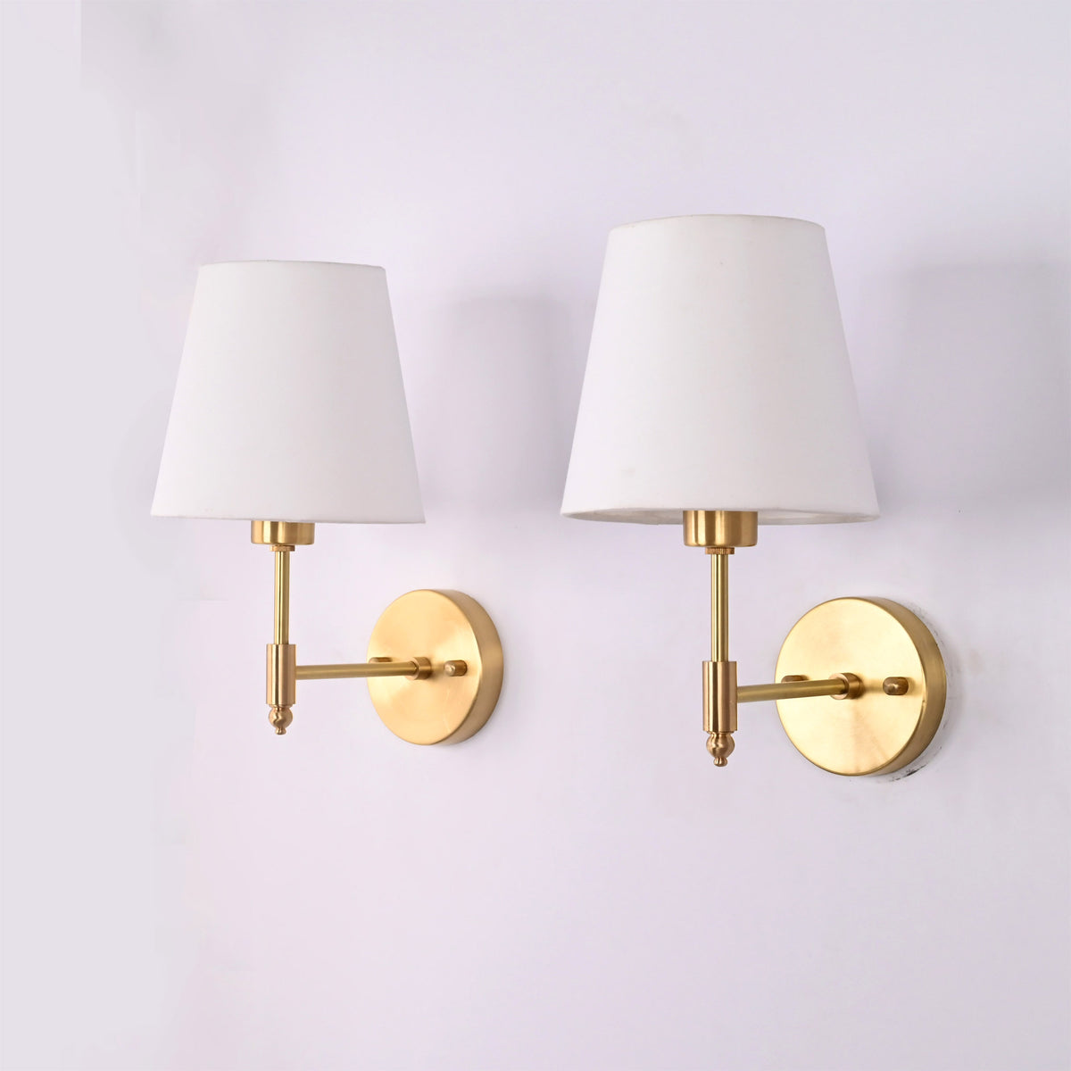 Pair of Milan brushed brass wall sconces with white fabric shades shown from an angled perspective, highlighting the elegant brass finish and modern classic design.