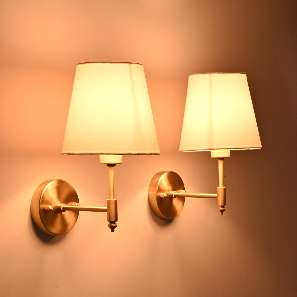 Pair of illuminated Milan white fabric shade brushed brass wall sconces creating a warm and elegant ambiance in a modern interior.