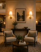 Milan brushed brass wall sconces with white fabric shades installed in a luxury hotel-style living room beside framed artwork and console table.