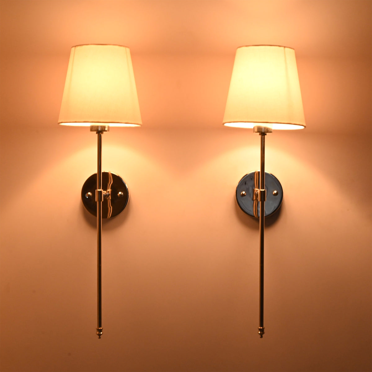 Evening illuminated view of Milan white shade chrome rod wall sconces with warm shade glow and elegant finish.