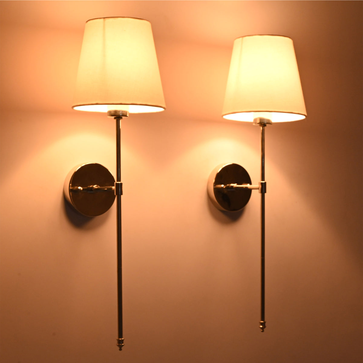 Soft light pair view of Milan white shade chrome rod sconces with warm wall reflection and polished backplates.