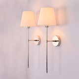 Illuminated pair of Milan white shade chrome wall sconces casting soft warm light on a plain wall.