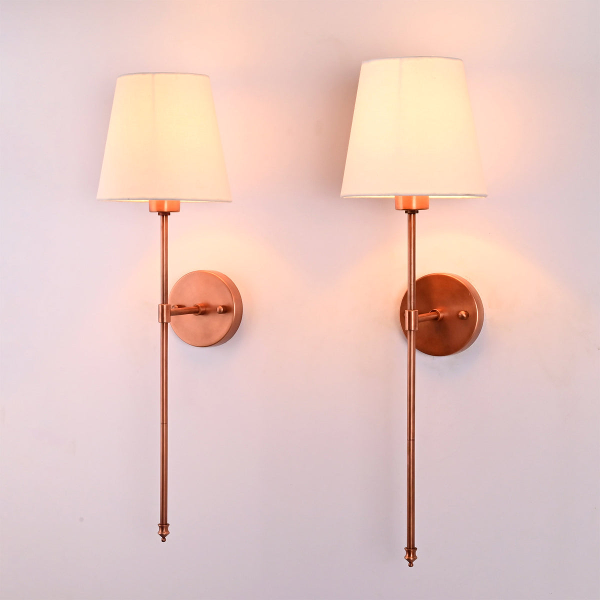 Angled view of Milan white shade copper rod wall sconces with warm glow and elegant rod profile.