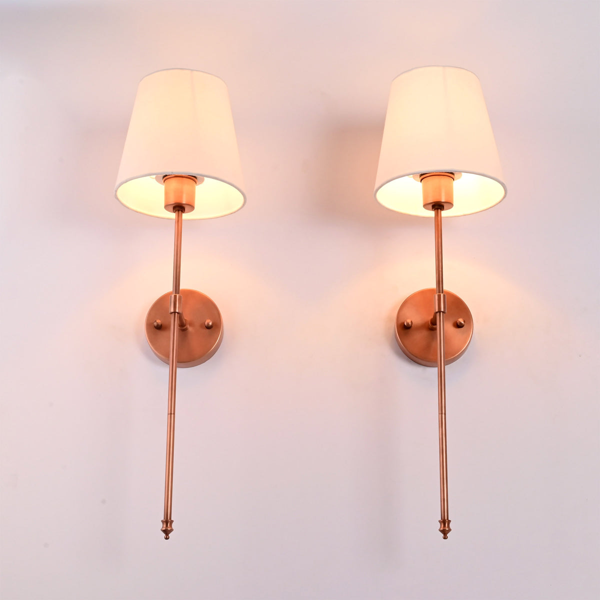 Illuminated front view of Milan white shade copper rod wall sconces casting soft warm ambient light.