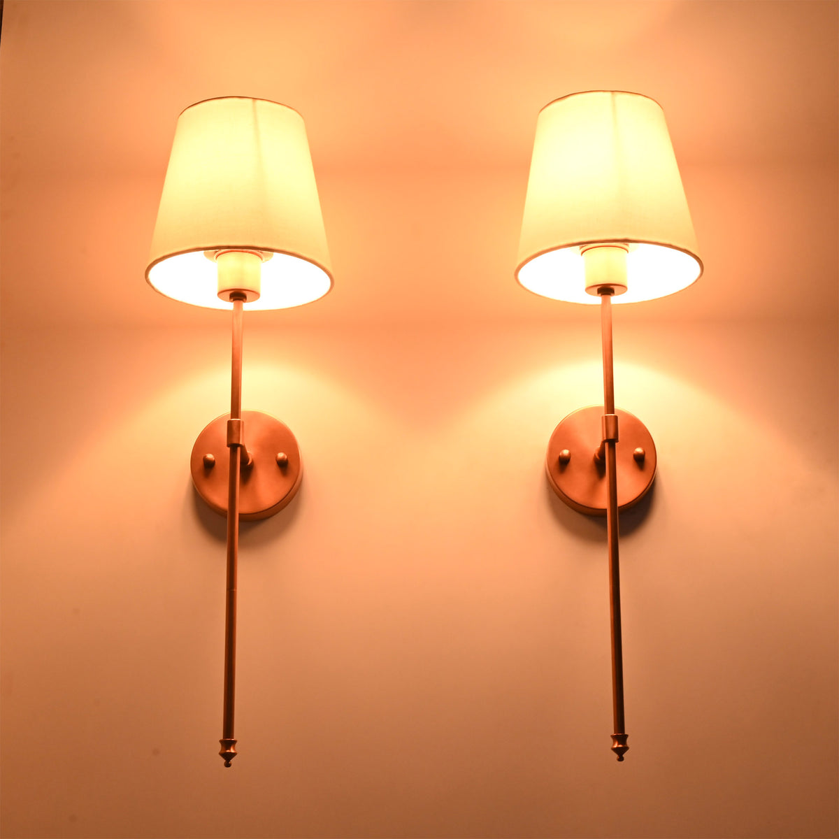 Warm lit detail view of Milan copper rod wall sconces with white tapered shades and slim frame.