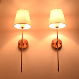 Warm lit detail view of Milan copper rod wall sconces with white tapered shades and slim frame.