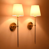 Angled view of Milan white shade wall sconces with tall rods and warm ambient evening glow.