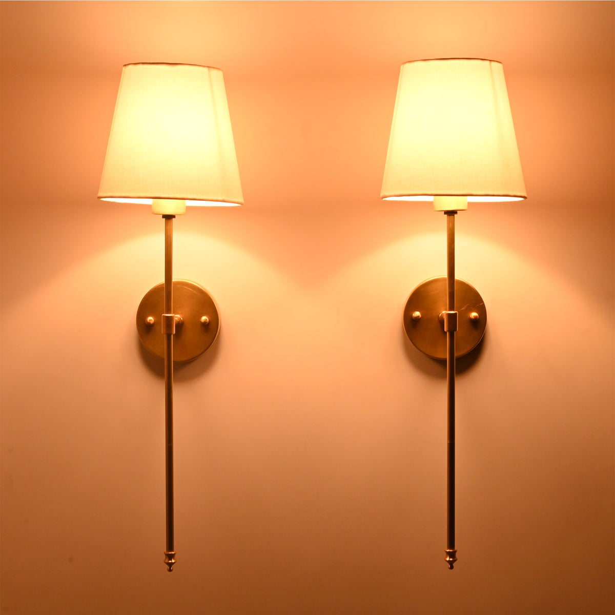White shade rod wall sconces glowing warmly on wall with soft upward and downward illumination.