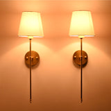 White shade rod wall sconces glowing warmly on wall with soft upward and downward illumination.