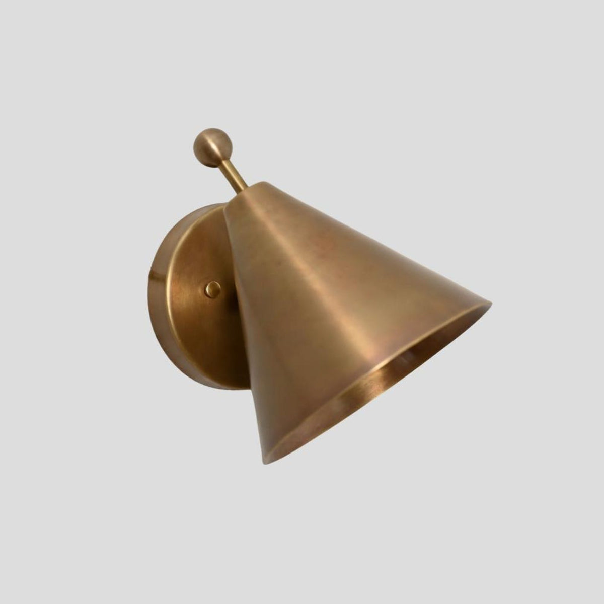 Minimalist solid brass cone sconce with ball accent, wall-mounted on a circular brass plate, side profile view.