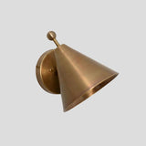 Minimalist solid brass cone sconce with ball accent, wall-mounted on a circular brass plate, side profile view.