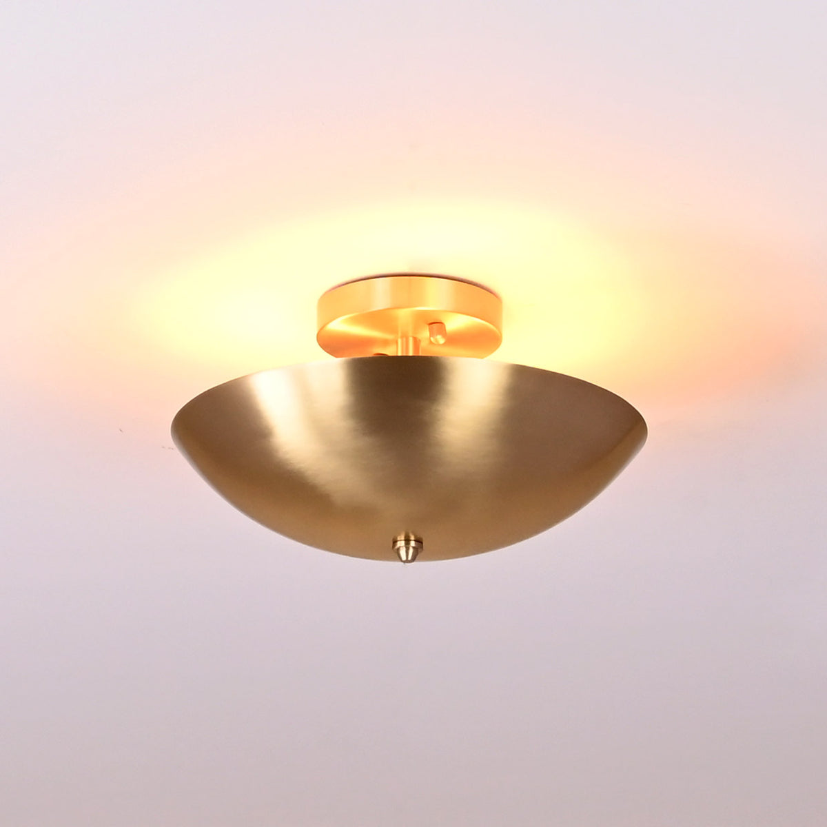 Modern minimalist brushed brass flushmount light radiating golden uplight against white ceiling