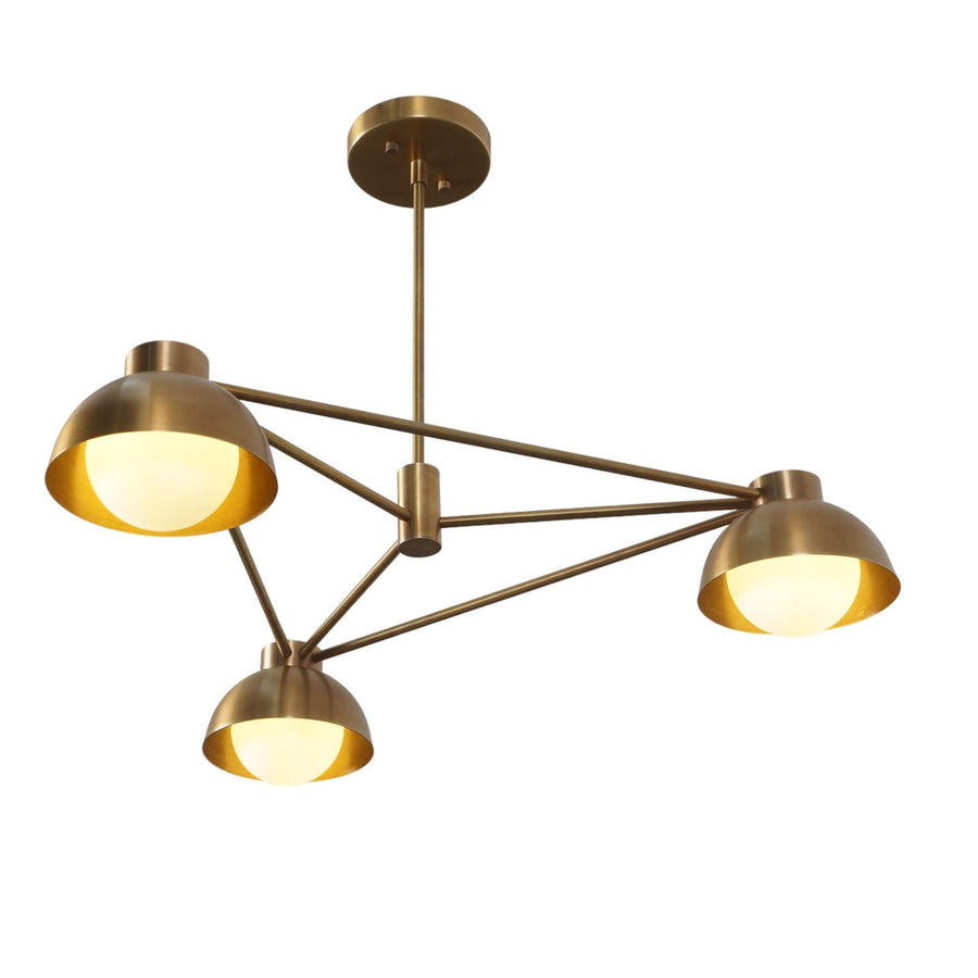 Three-light modern brass chandelier with dome shades and geometric arms, showcasing minimalist mid-century design and warm ambient illumination.
