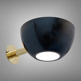 Black bowl wall sconce with polished brass arm turned on, showing a soft diffused light from the bottom opening.