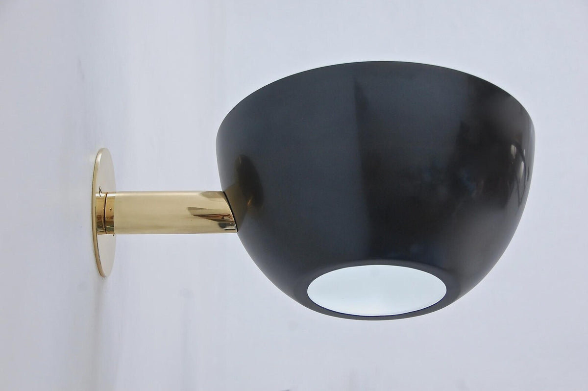 Side view of black bowl wall sconce mounted on a wall with a polished brass arm and round backplate.