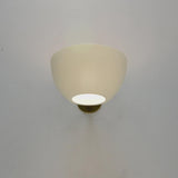 Centered white bowl wall sconce on a gray wall with warm diffused light and a brass mount visible beneath the shade.