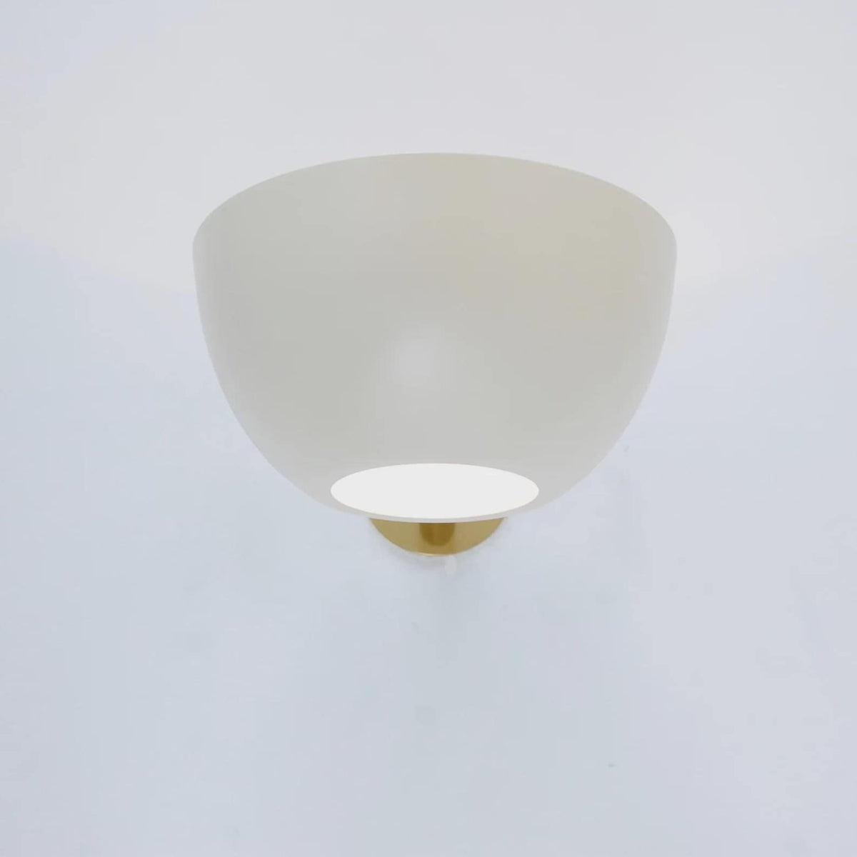 Front view of a matte white bowl wall sconce turned on, with a brass mounting plate partially visible behind.