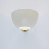 Front view of a matte white bowl wall sconce turned on, with a brass mounting plate partially visible behind.