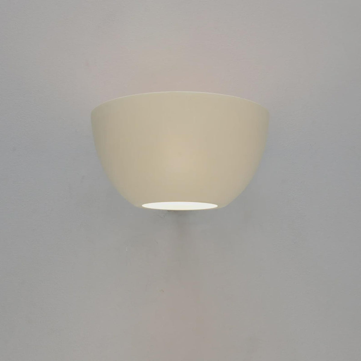 White bowl wall sconce mounted on a gray wall, emitting a soft downward glow from the bottom opening.