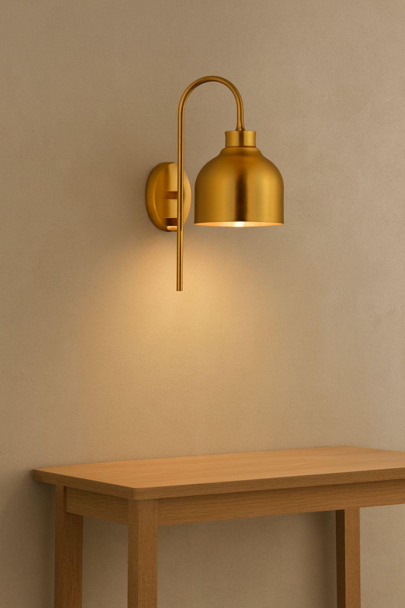 Modern brass wall sconce with dome bell shade mounted above a wooden console table, casting a warm ambient glow on a beige wall.