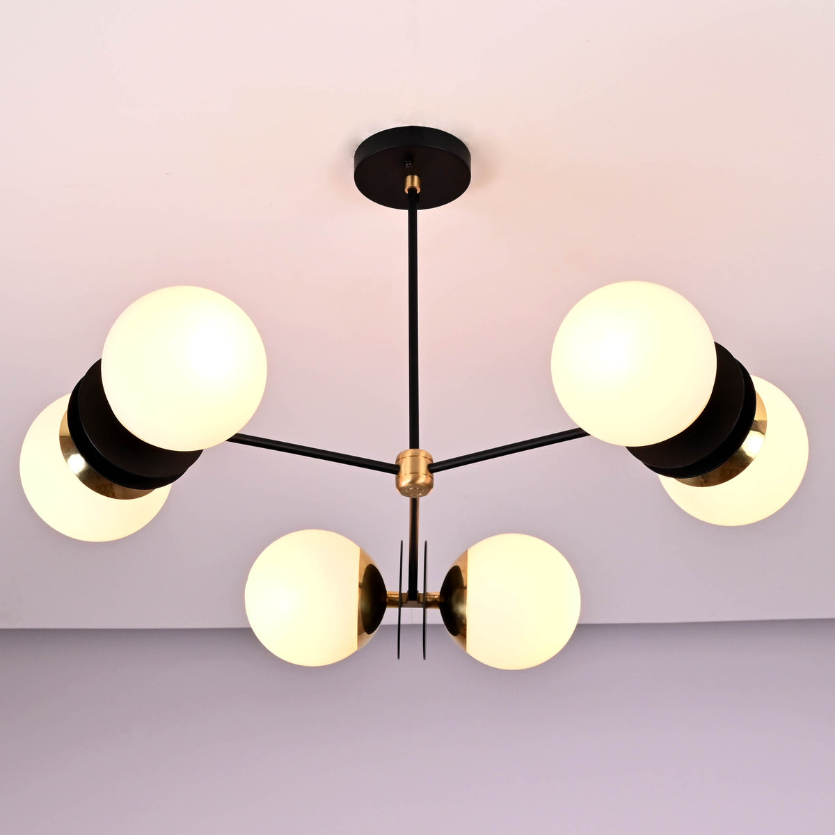 Elegant chandelier with 6 opal glass globes, matte black rods, and polished brass accents, installed on a ceiling for modern interiors.