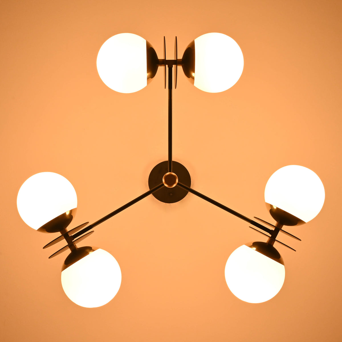 Ceiling chandelier with 6 opal glass globes glowing warmly, brass accents, and black structure, viewed from below.